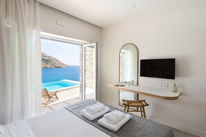 A hotel room with a bed, a desk with a mirror, a TV, and a view of the sea.