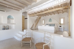 A spacious room with a large bed, a staircase, and two chairs.