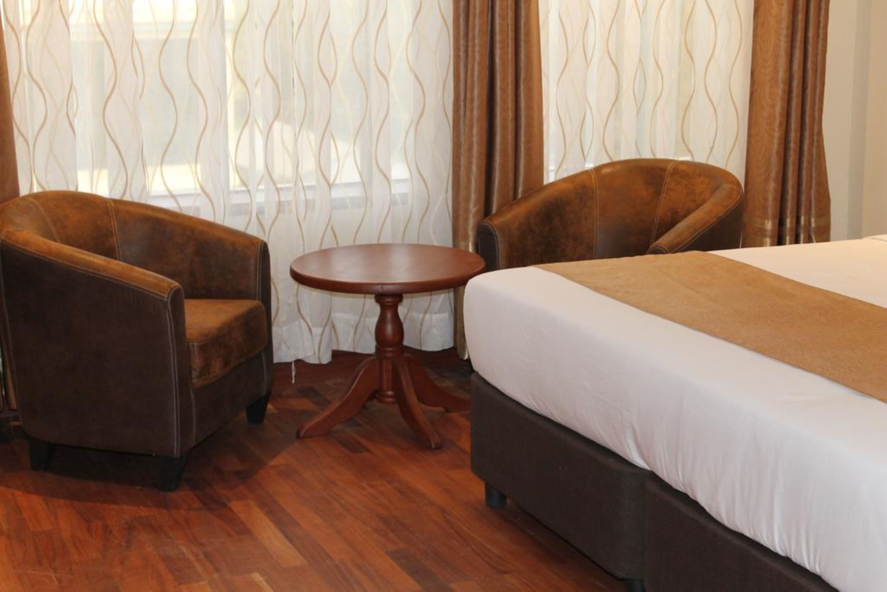 A hotel room with a bed, two armchairs, and a small round table.