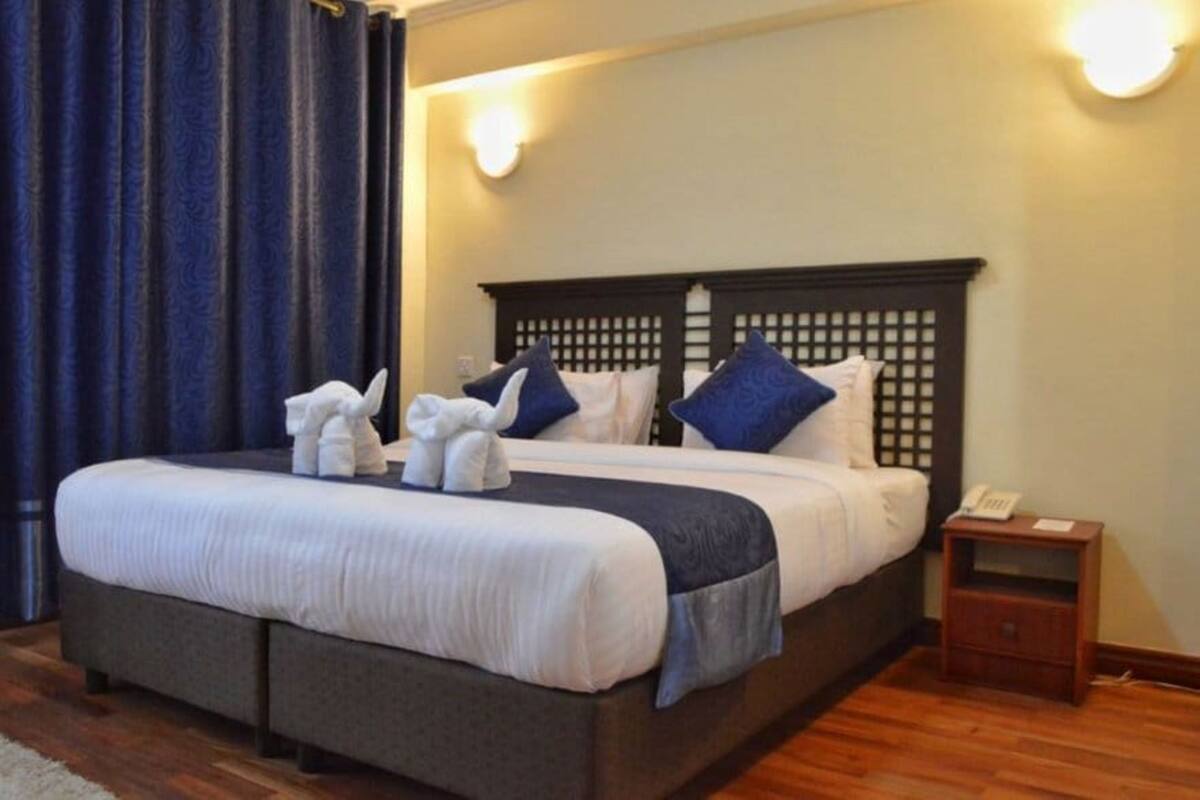 A neatly made bed with a dark headboard, white linens, and blue pillows. There is a small bedside table with a lamp and a phone.