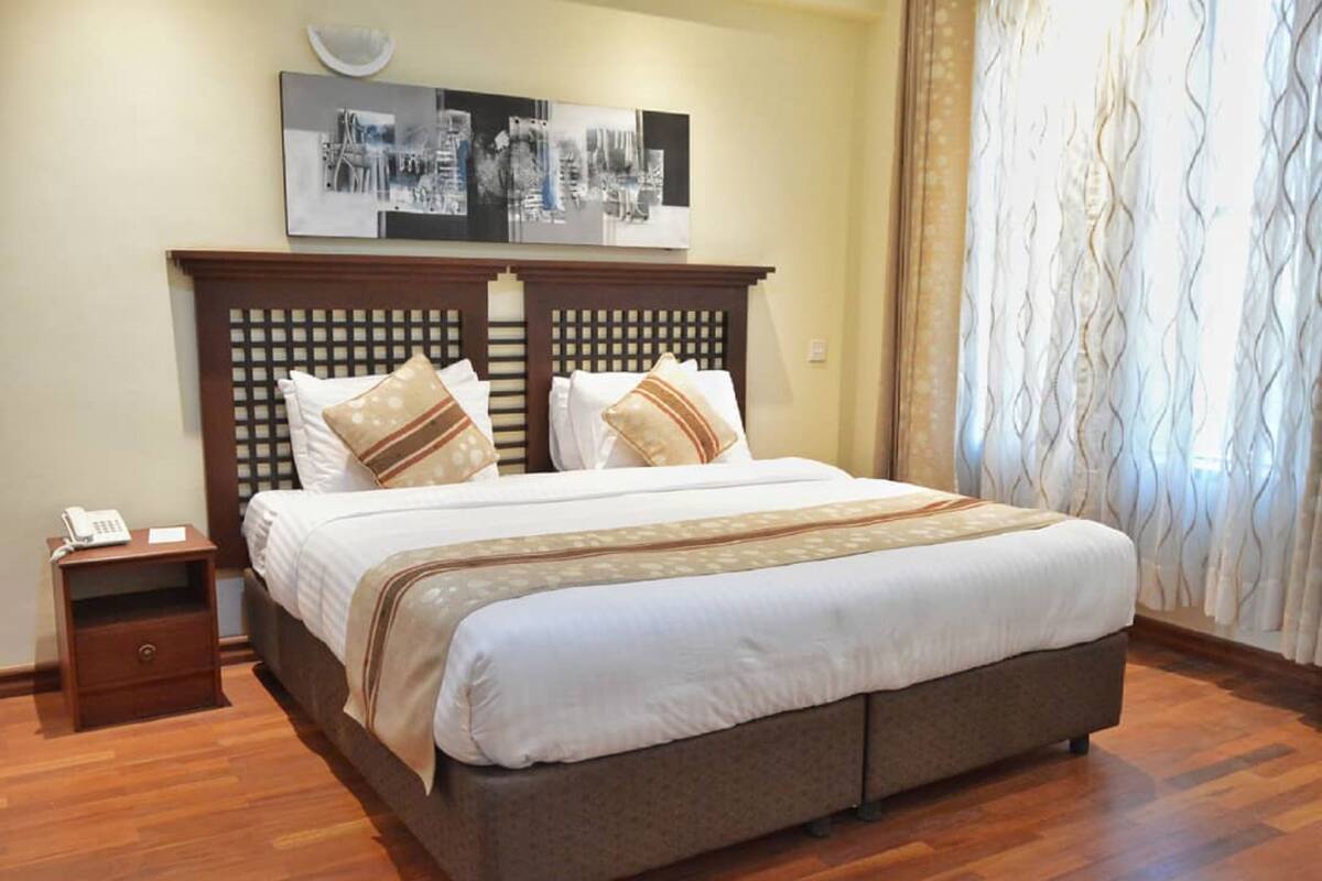 A neatly made bed with a wooden headboard, a bedside table with a phone, and a wall-mounted artwork above the bed.