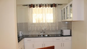 A small kitchen with white cabinets, a black countertop, a microwave, and a kettle. - Cranes Suites Hotel (Kitale)
