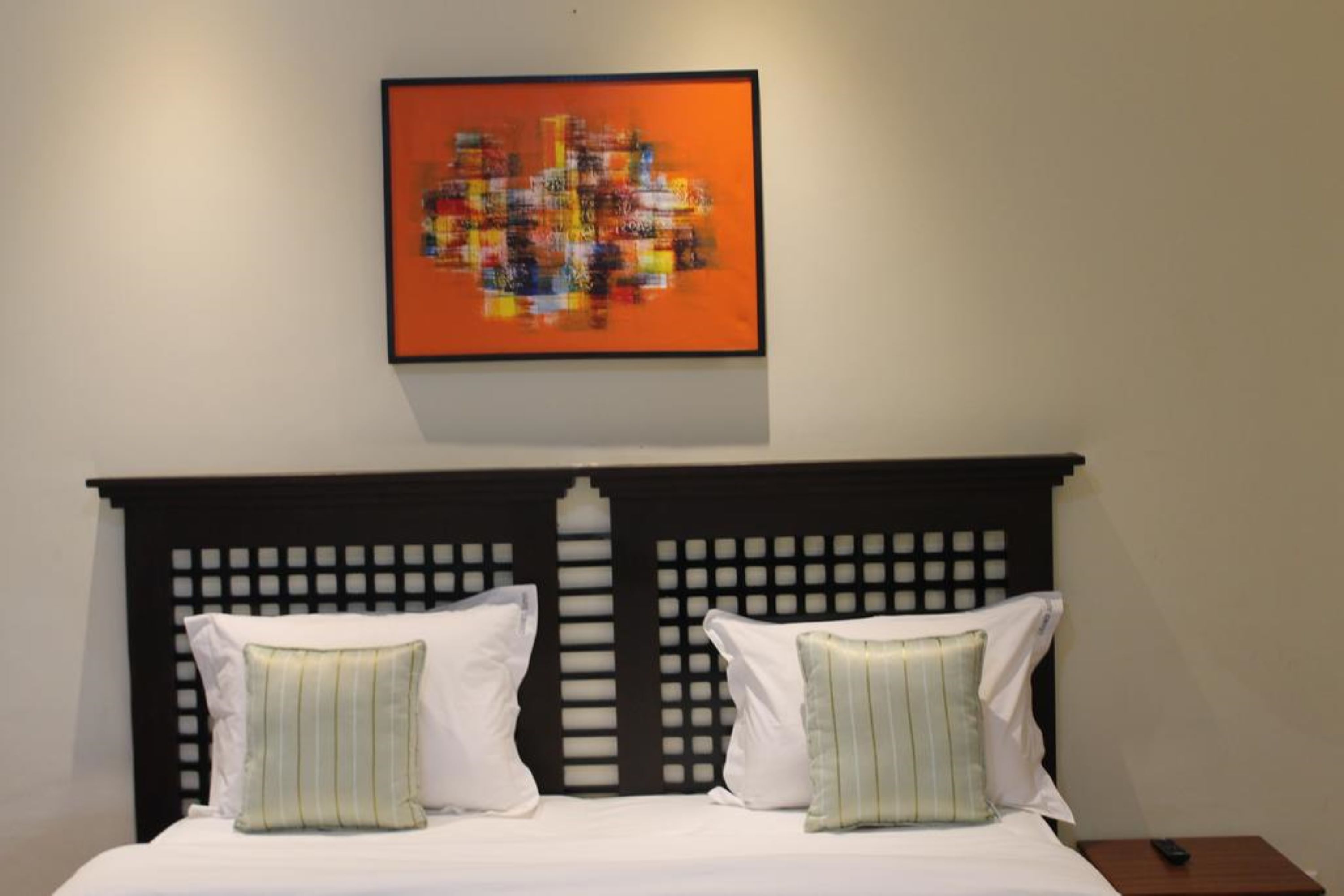 Una habitación de hotel con una cama, dos almohadas, un cabecero y una obra de arte enmarcada en la pared.