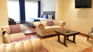A hotel room with a bed, two sofas, a coffee table, and a TV. - Cranes Suites Hotel (Kitale)