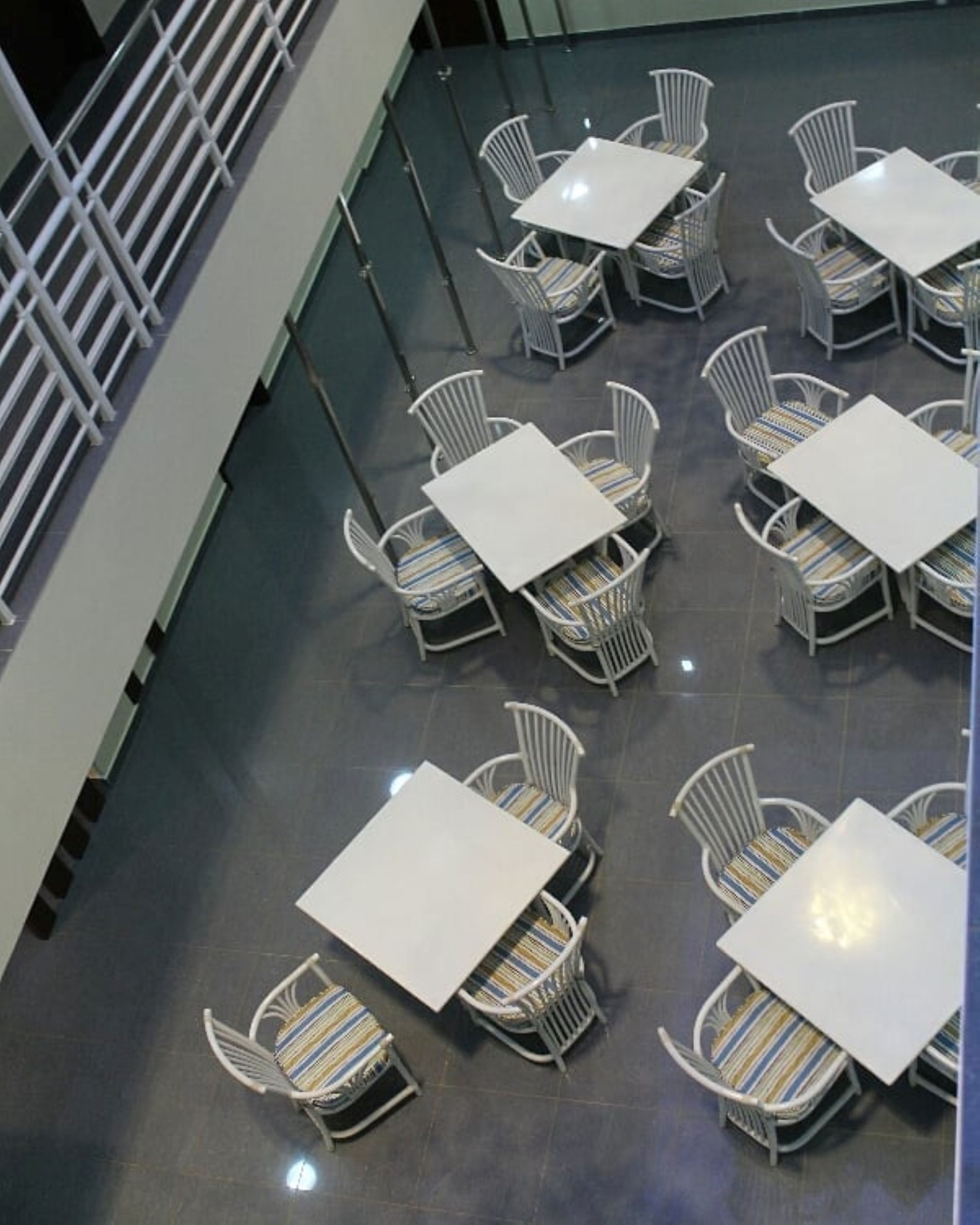 A spacious indoor area with multiple white tables and chairs arranged in a grid pattern.