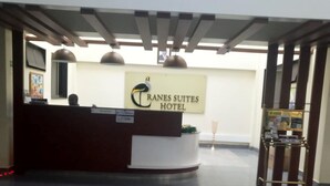 A hotel reception area with a reception desk, a sign for 'Tranes Suites Hotel', and a cart with brochures. - Cranes Suites Hotel (Kitale)