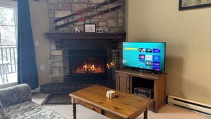 A living room with a stone fireplace, a television, a wooden coffee table, and a patterned sofa. - Stunning 2 bed Condo in Les Manoirs, Mont-Tremblant (Mont-Tremblant)