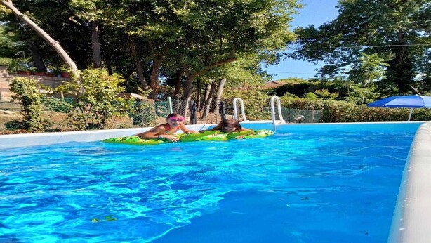 Ein Freibad mit klarem, blauem Wasser, umgeben von Bäumen und einem Zaun.