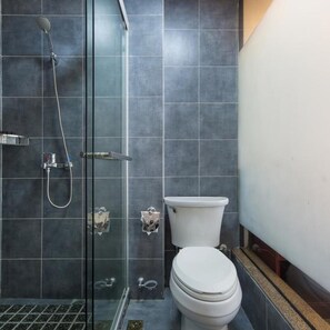 A bathroom with a glass shower enclosure, a white toilet, and a tiled floor.