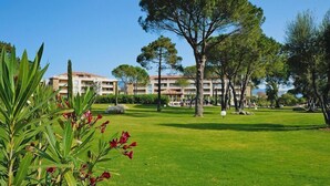 Un patio de hotel con un césped cuidado, varios árboles y un edificio al fondo.