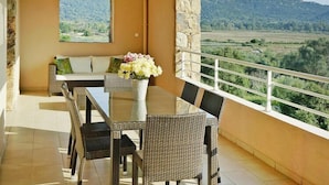 Un balcón con mobiliario de mimbre, una mesa de vidrio y un jarrón con flores.