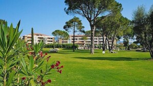 A hotel with a well-maintained lawn, trees, and a building with multiple balconies. - Apartment in Corsica near Palombaggia Beach (Porto-Vecchio)