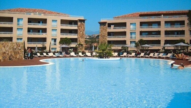 A hotel with a large swimming pool surrounded by lounge chairs and a building with multiple balconies. - Apartment in Corsica near Palombaggia Beach (Porto-Vecchio)