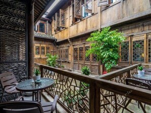 A traditional wooden building with multiple rooms, a balcony with seating, and a large tree.
