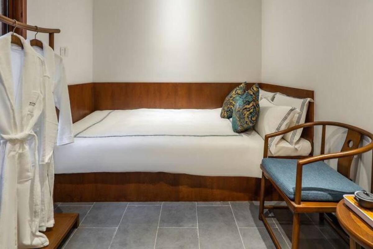 Une petite chambre à coucher, bien rangée, avec un lit simple, une tête de lit en bois, une table de chevet avec une lampe et une chaise.