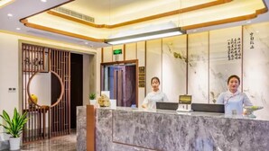 Ein Hotel-Rezeptionsbereich mit Marmor-Theke, zwei Rezeptionisten, einer Wand mit Kalligraphie und einem traditionellen Tor.
