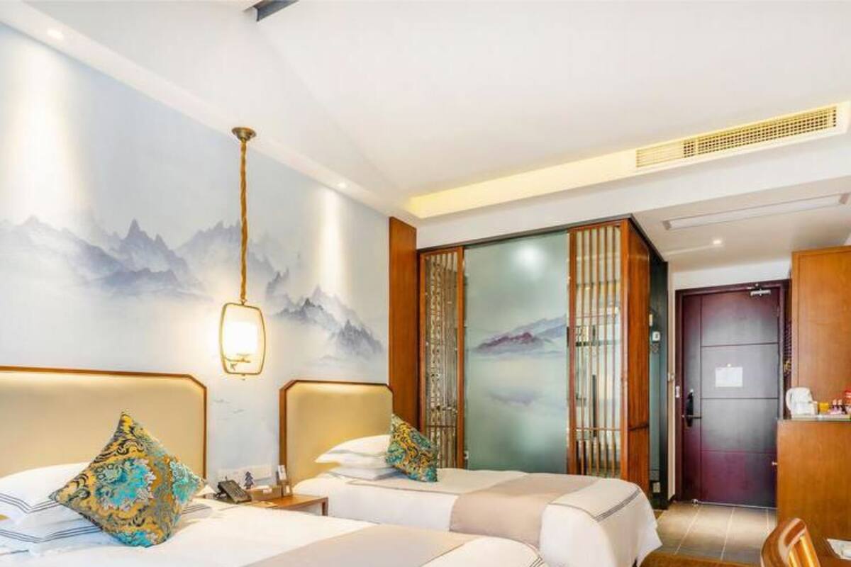 Une chambre d’hôtel avec deux lits, un plancher en bois, un bureau et un mur orné d’un tableau représentant une montagne.