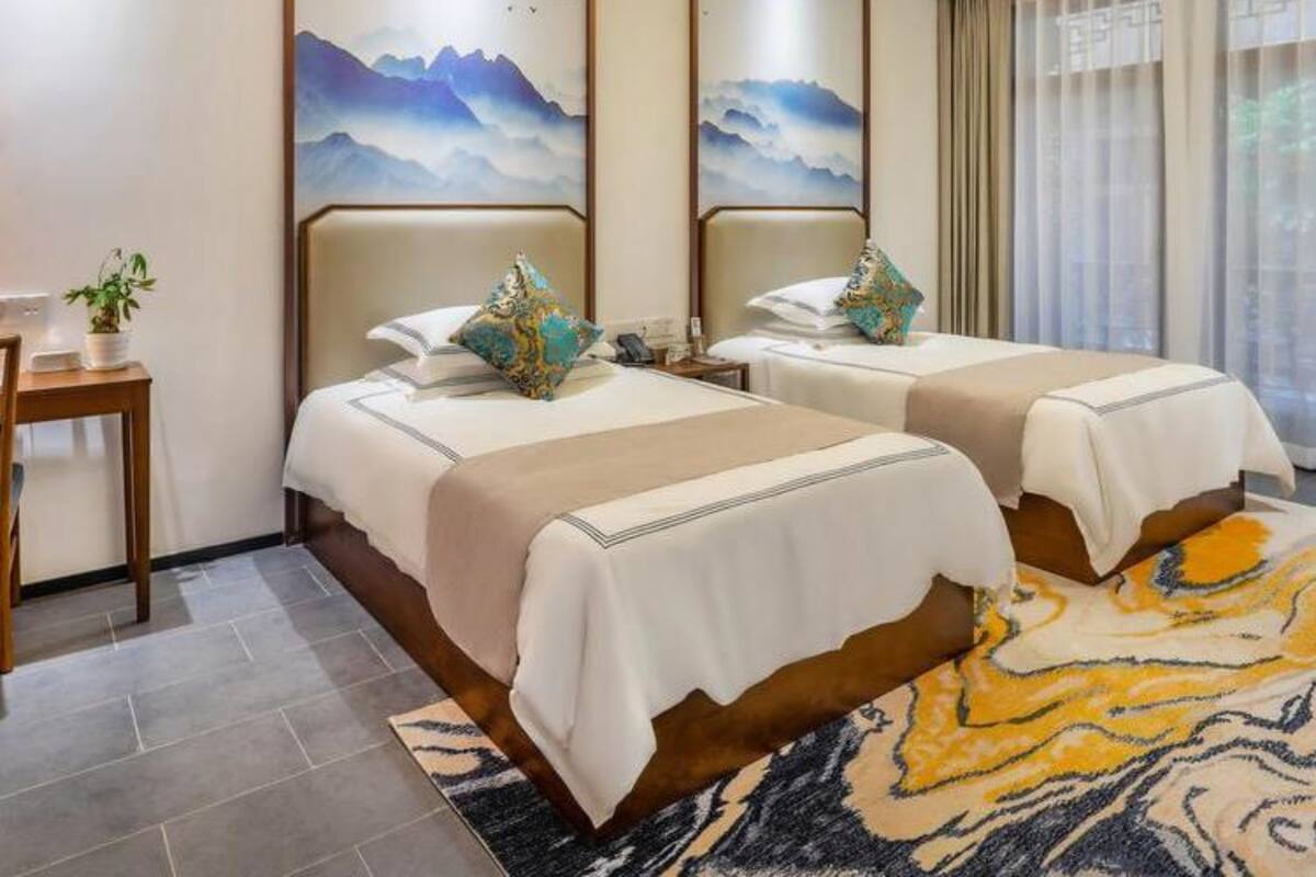 Une chambre d’hôtel avec deux lits, un bureau et une grande fenêtre avec des rideaux.