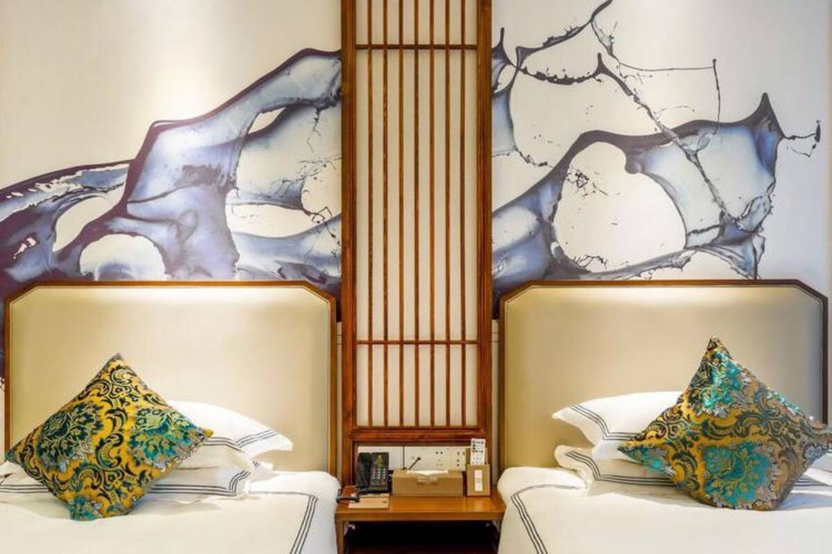 Une chambre d’hôtel avec deux lits, chacun agrémenté d’un coussin à motifs, d’un séparateur en panneaux de bois et d’œuvres d’art murales abstraites.