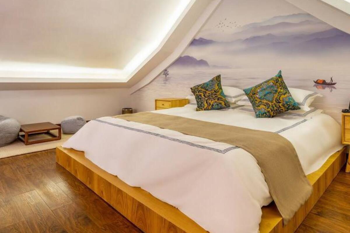 Une chambre avec un plafond en pente, un lit agrémenté d’oreillers à motifs, une tête de lit en bois et une table de chevet.