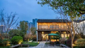 Ein traditionelles Gebäude mit Ziegeldach und Holzfassade, umgeben von einem gepflegten Garten mit Steinwegen und viel Grün.