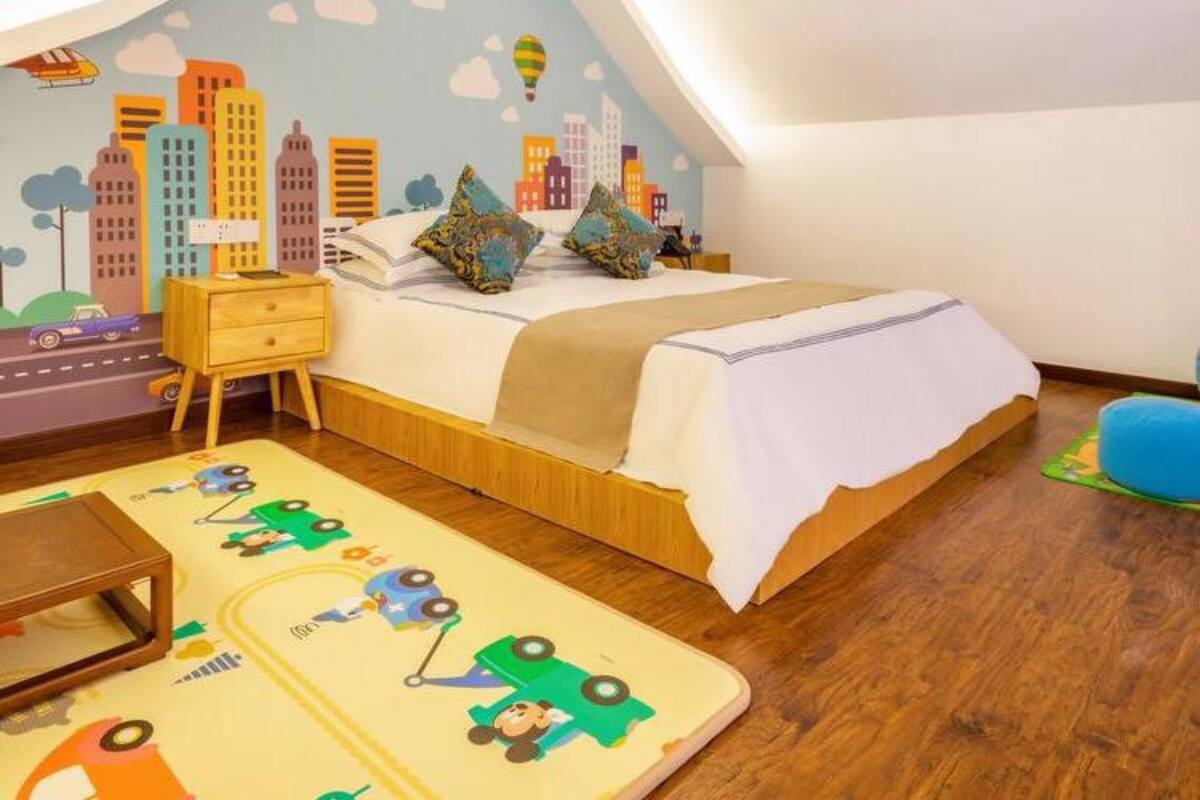 Une chambre d’enfant avec une fresque représentant un paysage urbain, un lit, une table de chevet et un tapis représentant une voiture jouet.