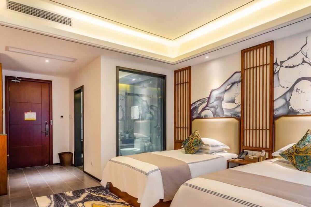 Une chambre d’hôtel avec deux lits, une grande peinture abstraite au mur, une porte en bois et un tapis à motifs.