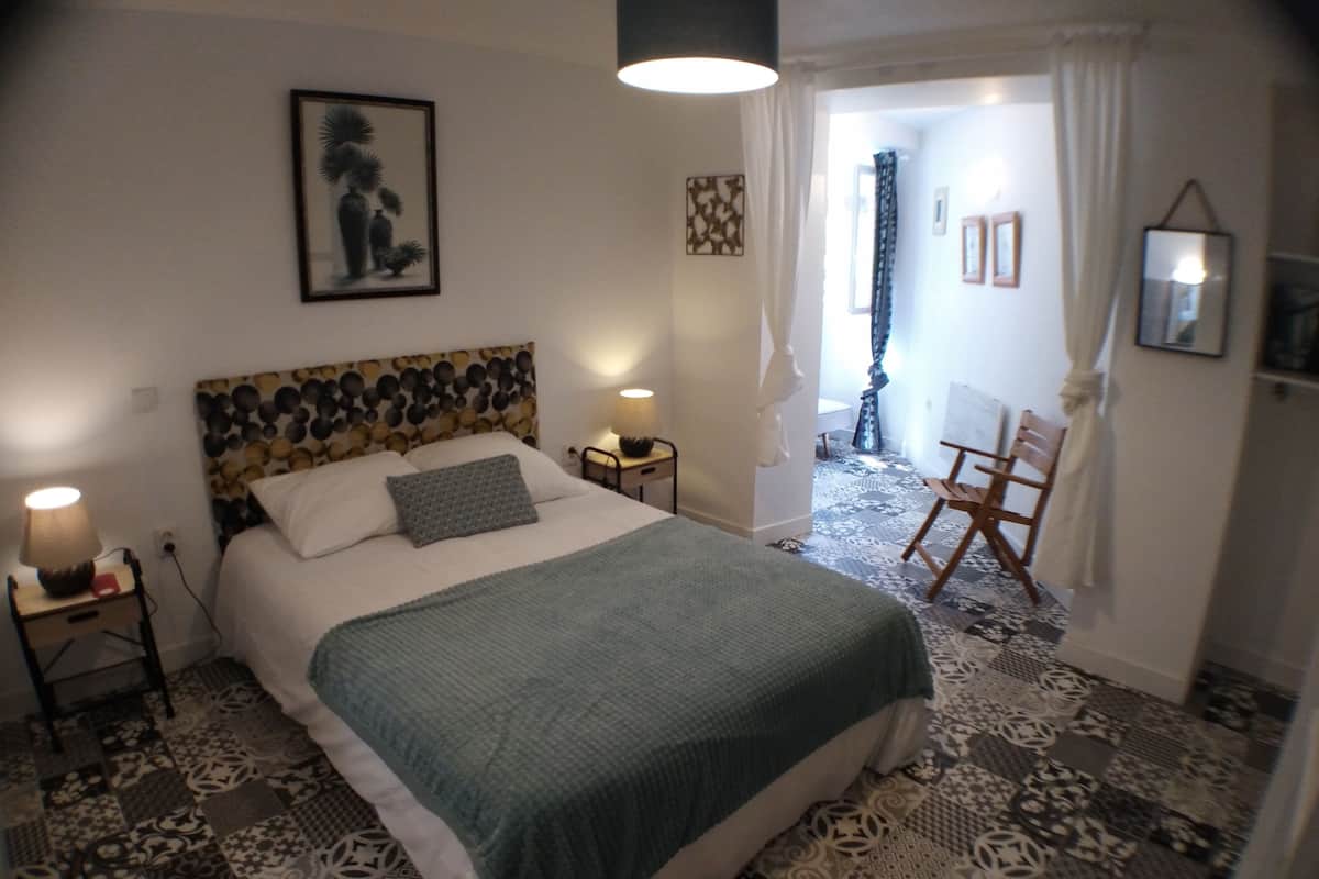 Een slaapkamer met een kamer met een patroon vloer, een bed met een groene deken, twee nachtlampjes en een ingelijst foto aan de muur.