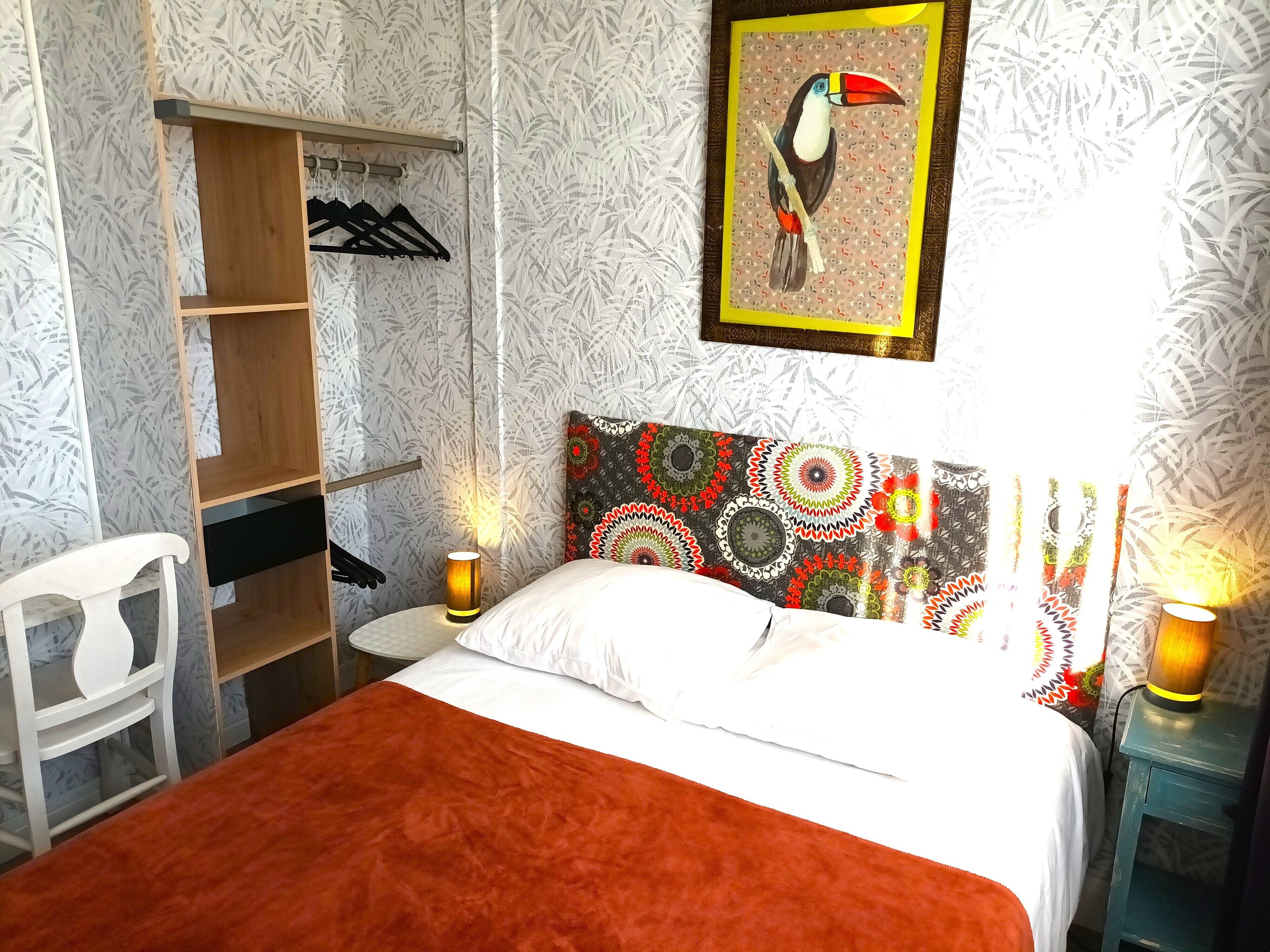 A bedroom with a bed, a wooden wardrobe, a chair, and a wall-mounted picture.