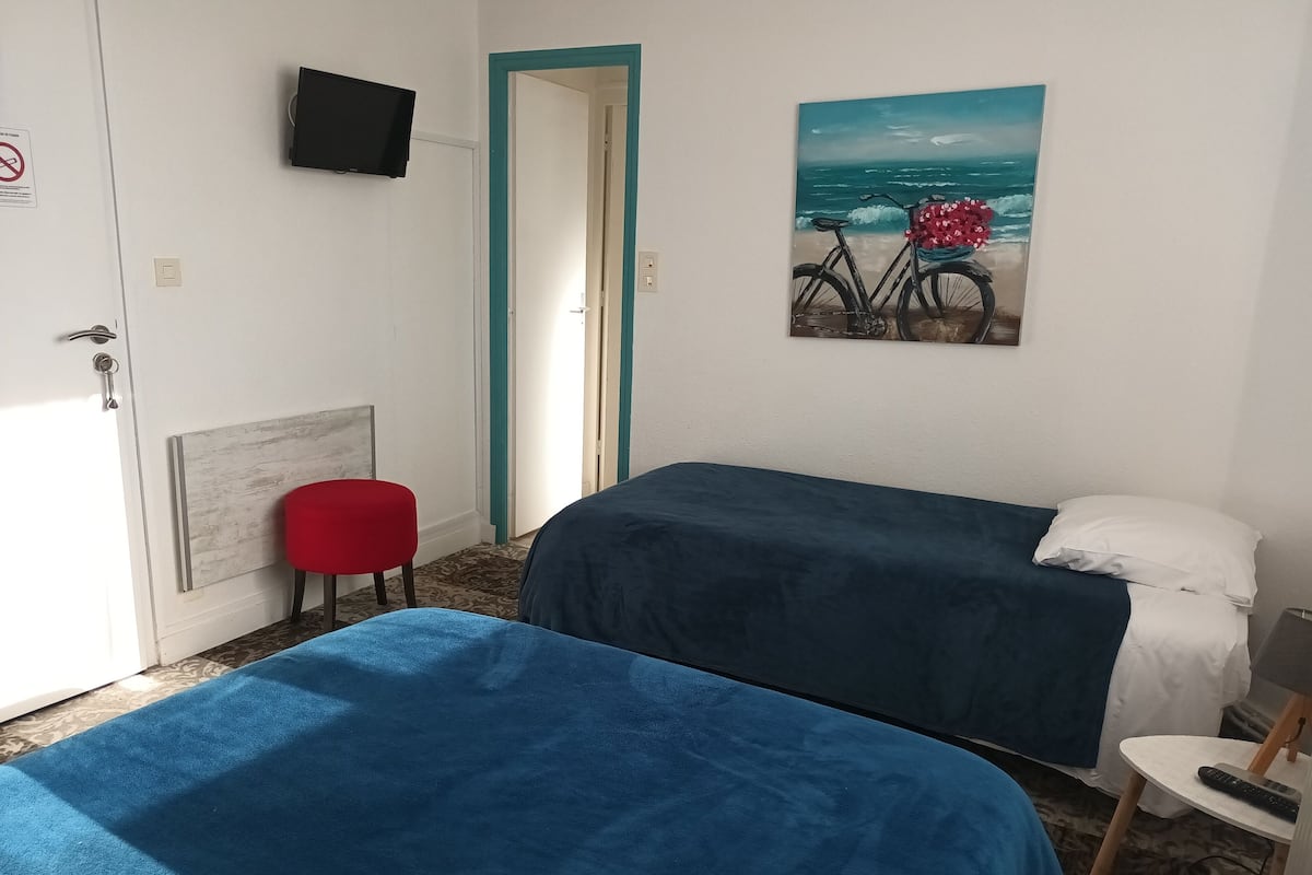 Een kamer met twee bedden, een rode stoel, een schilderij van een fiets aan de muur en een televisie boven een deur.