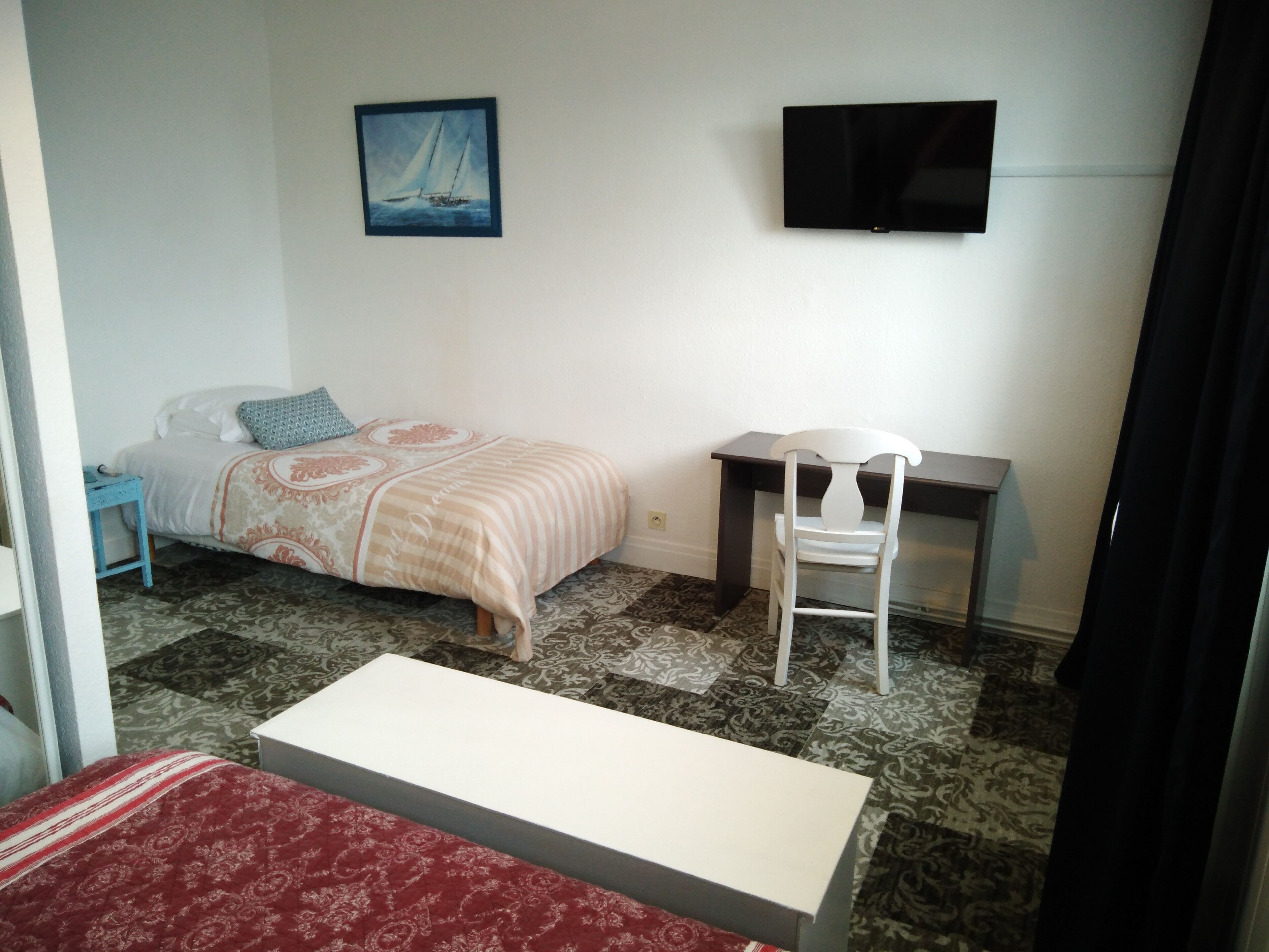 A bedroom with a bed, a desk, a chair, a TV, and a painting on the wall.