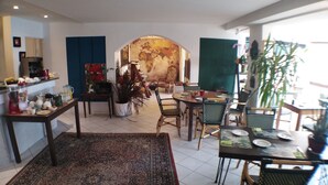 Un comedor con una mesa redonda, sillas y un tapete grande. Hay una zona de cocina con varios electrodomésticos y un refrigerador.