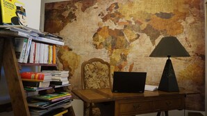 Un salón de estudio con un escritorio de madera, una computadora portátil, una lámpara y una estantería llena de libros.