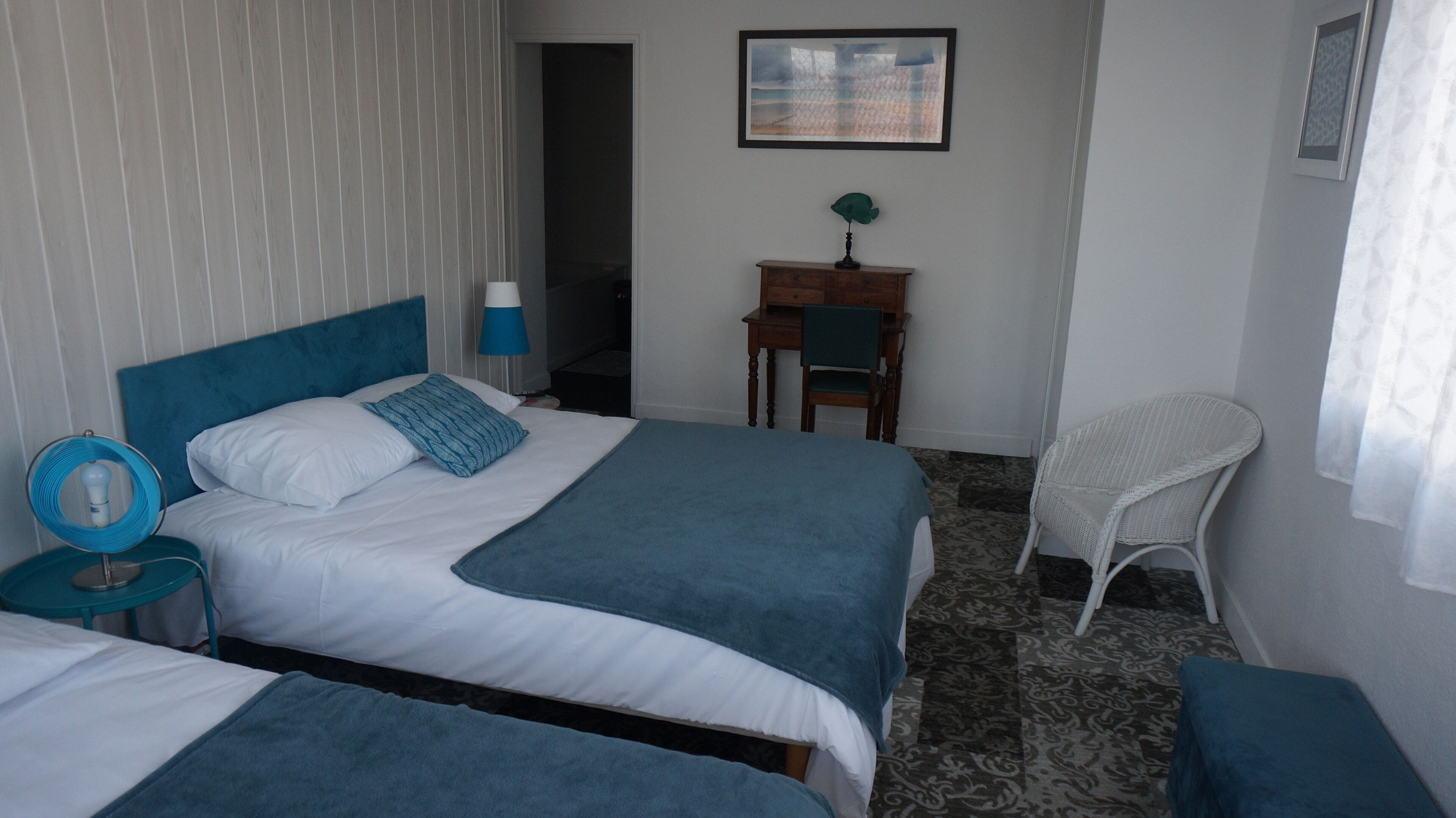 Une chambre d’hôtel avec deux lits, un bureau, une chaise et une fenêtre avec des rideaux.