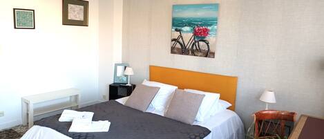 A hotel room with a bed, a nightstand, a chair, and a painting of a bicycle on a wall.