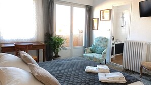 A bedroom with a bed, a chair, a desk, a radiator, and a window with curtains. - Le Vent des Globes (Les Sables-d'Olonne)