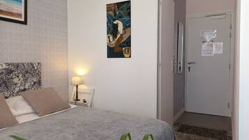 Una habitación de hotel con una cama, una mesita de noche con una lámpara, una obra de arte colgada en la pared, una puerta con espejo y un cartel, y una alfombra estampada.