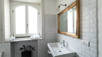Un baño con paredes de ladrillo blanco, un lavamanos blanco, un espejo con marco de madera y una ventana con una toalla blanca en el alféizar.