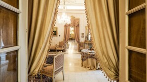 Un vaste hall d’entrée agrémenté de rideaux richement décorés, d’un lustre et d’un espace repas comprenant une table et des chaises.