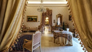 Une chambre luxueuse, ornée d’un lustre, avec une table à manger recouverte d’une nappe à motifs floraux et un grand miroir.