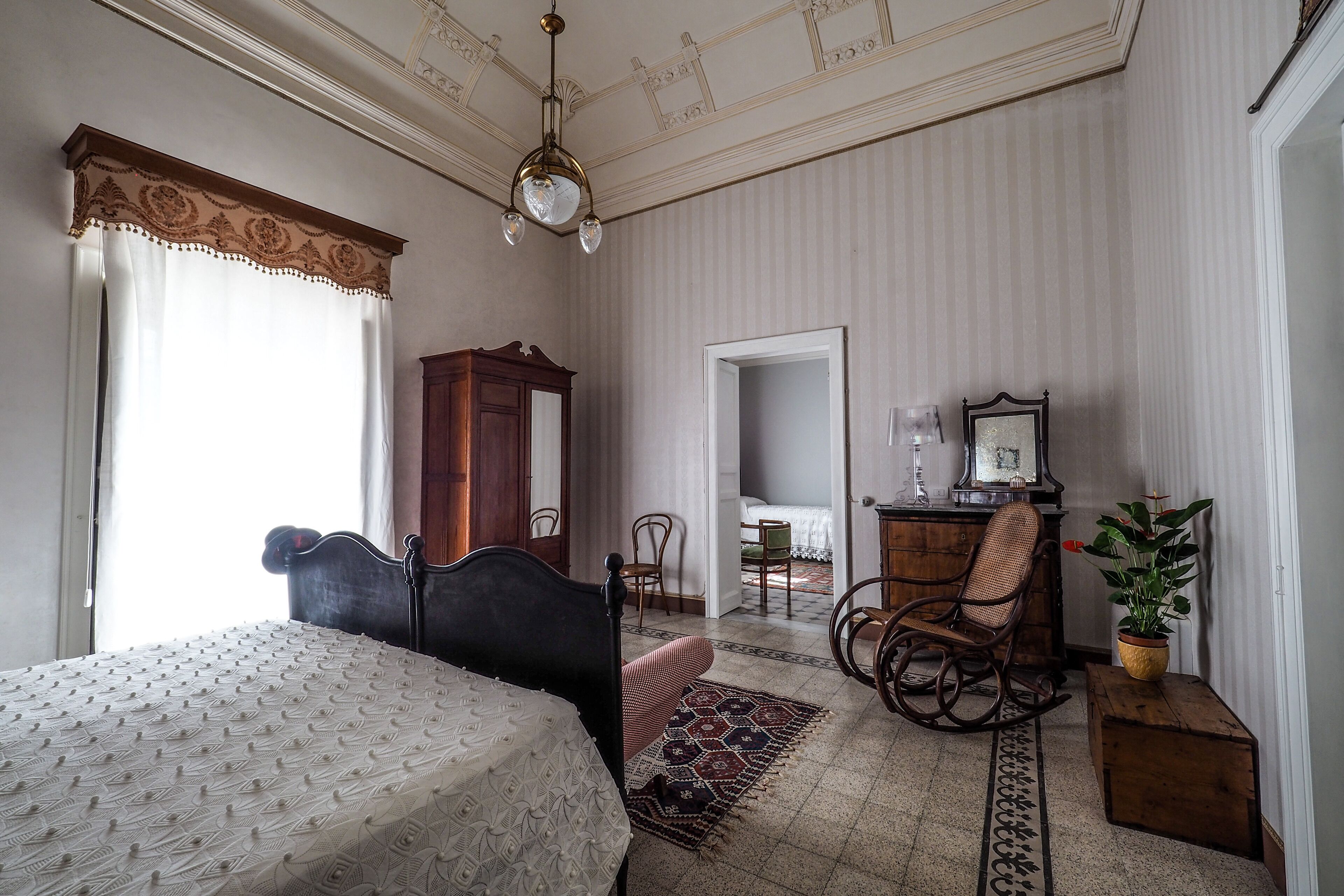 A bedroom with a bed, a rocking chair, a dresser, and a mirror.