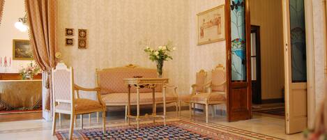 A traditional room with a patterned carpet, a sofa, two armchairs, a small table with a vase of flowers, and a door with a stained glass design.