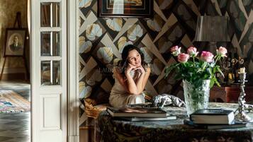Una habitación con papel tapiz estampado, un cuadro en la pared, un florero con flores sobre una mesa y una lámpara.