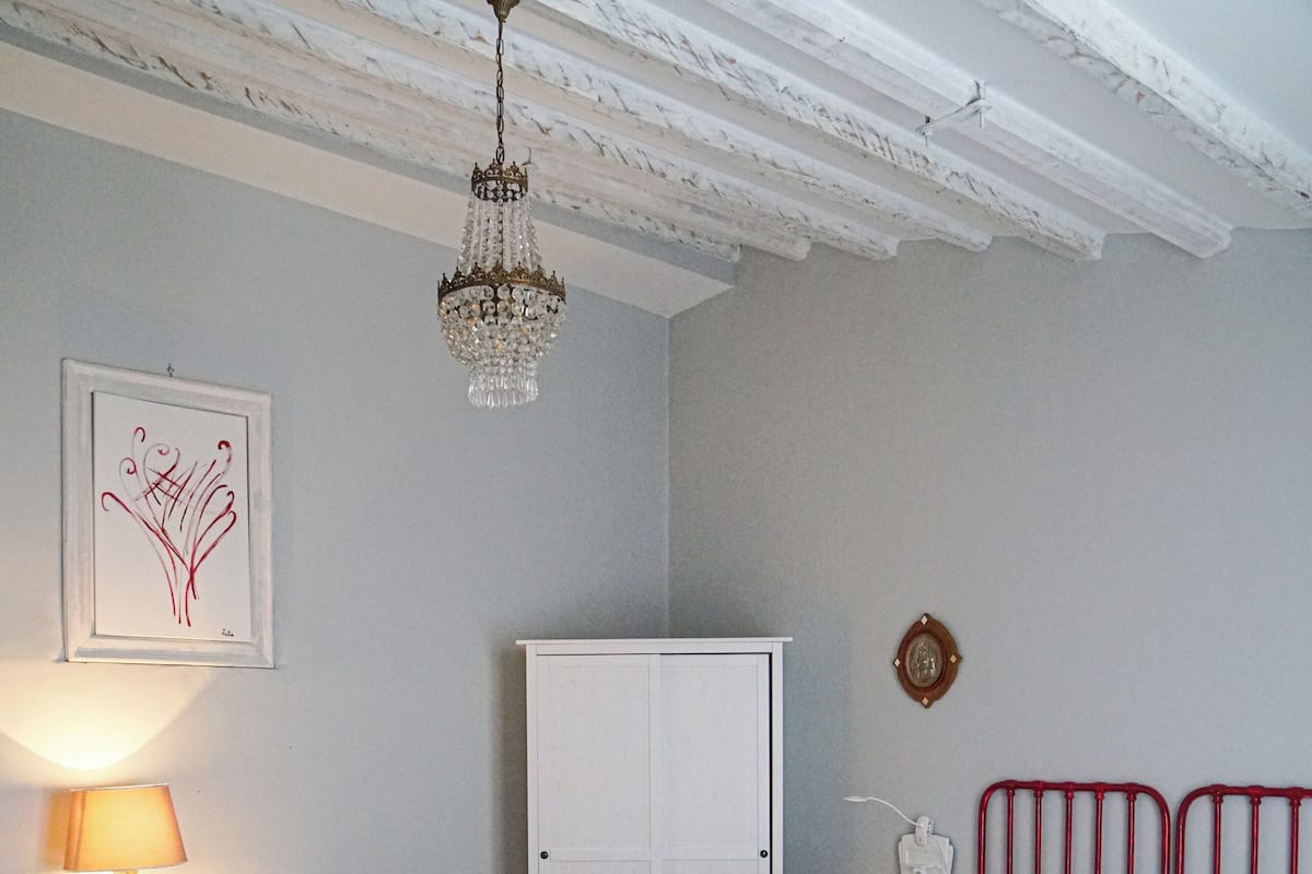 Une chambre avec un sol à carreaux, un lit avec une literie blanche et des oreillers rouges, un bureau avec une lampe et un lustre.