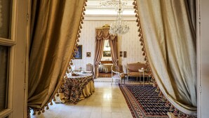 Une chambre luxueuse avec un grand lit, des rideaux richement décorés, un lustre et un tapis à motifs.