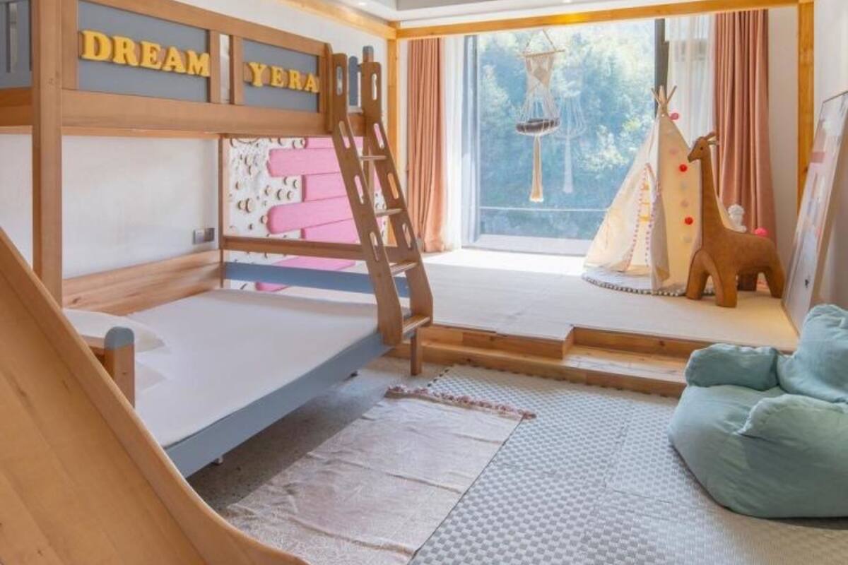 Une chambre d’enfant avec un lit superposé, un toboggan et une fenêtre donnant sur l’extérieur.