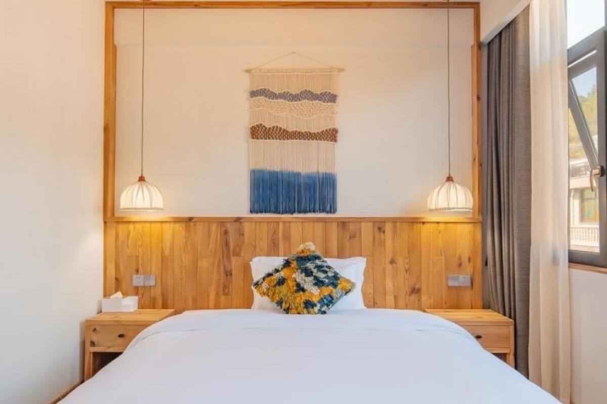 Une chambre à coucher avec un grand lit, une tête de lit en bois, deux tables de chevet, une tapisserie murale et une fenêtre avec des rideaux.