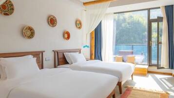 A hotel room with two beds, a balcony with a view, and decorative plates on the wall.
