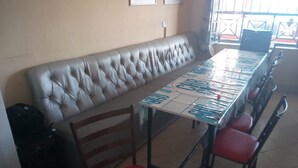 A long table with a white tablecloth and red chairs, a cushioned bench, and a speaker in the corner.