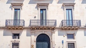 En bygningsfacade med tre balkoner, en midtertilmuret buesgang og et lille vindue med metalgitter.